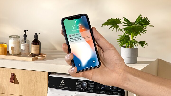 En hand håller en mobiltelefon som visar Electrolux app för uppkopplade vitvaror.